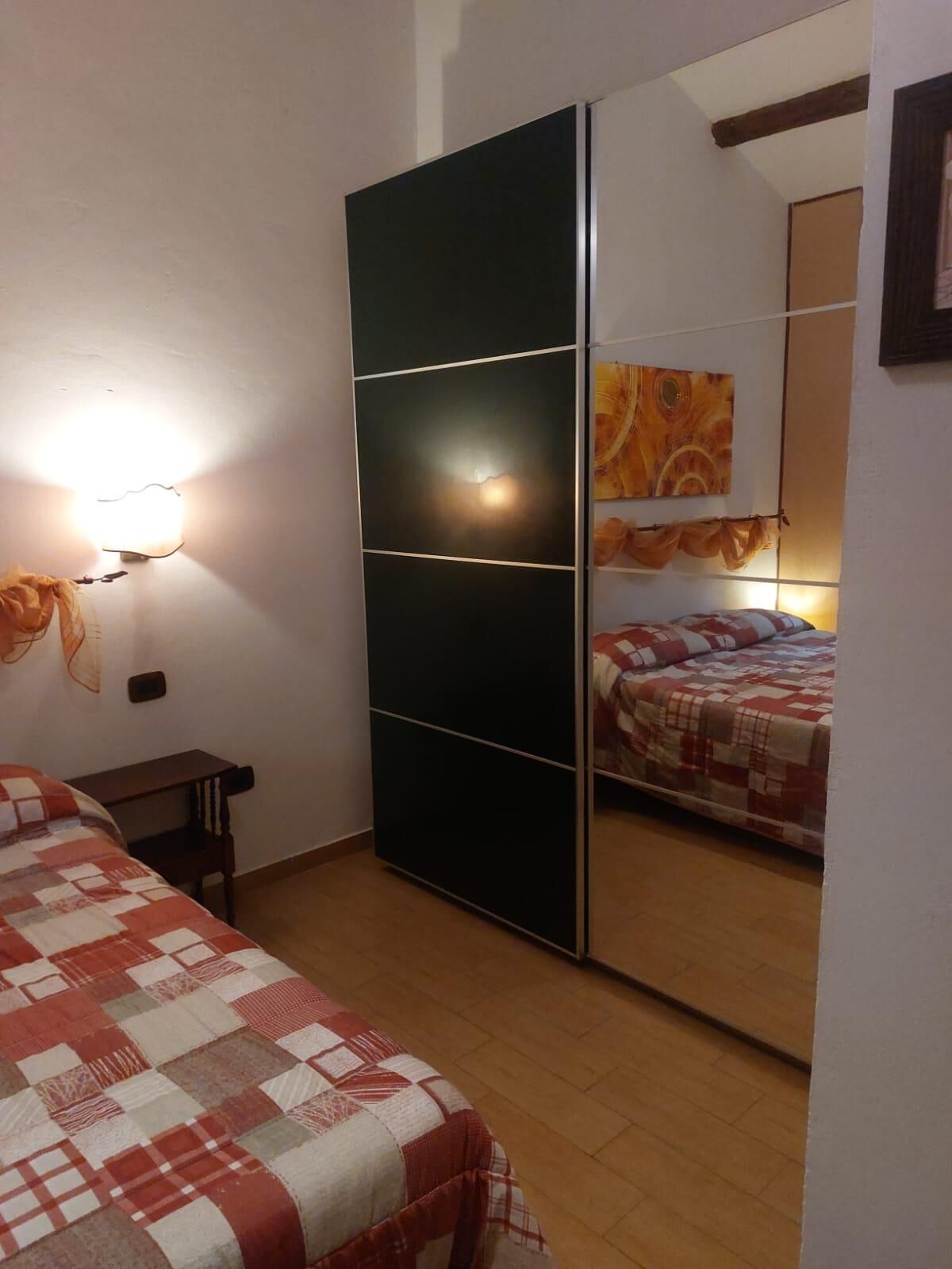 A bedroom with a bed, a wardrobe, a desk, and a mirror.