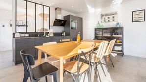 Une cuisine moderne avec un coin repas, comprenant une table et des chaises en bois, un four encastré et un meuble avec une porte en verre.