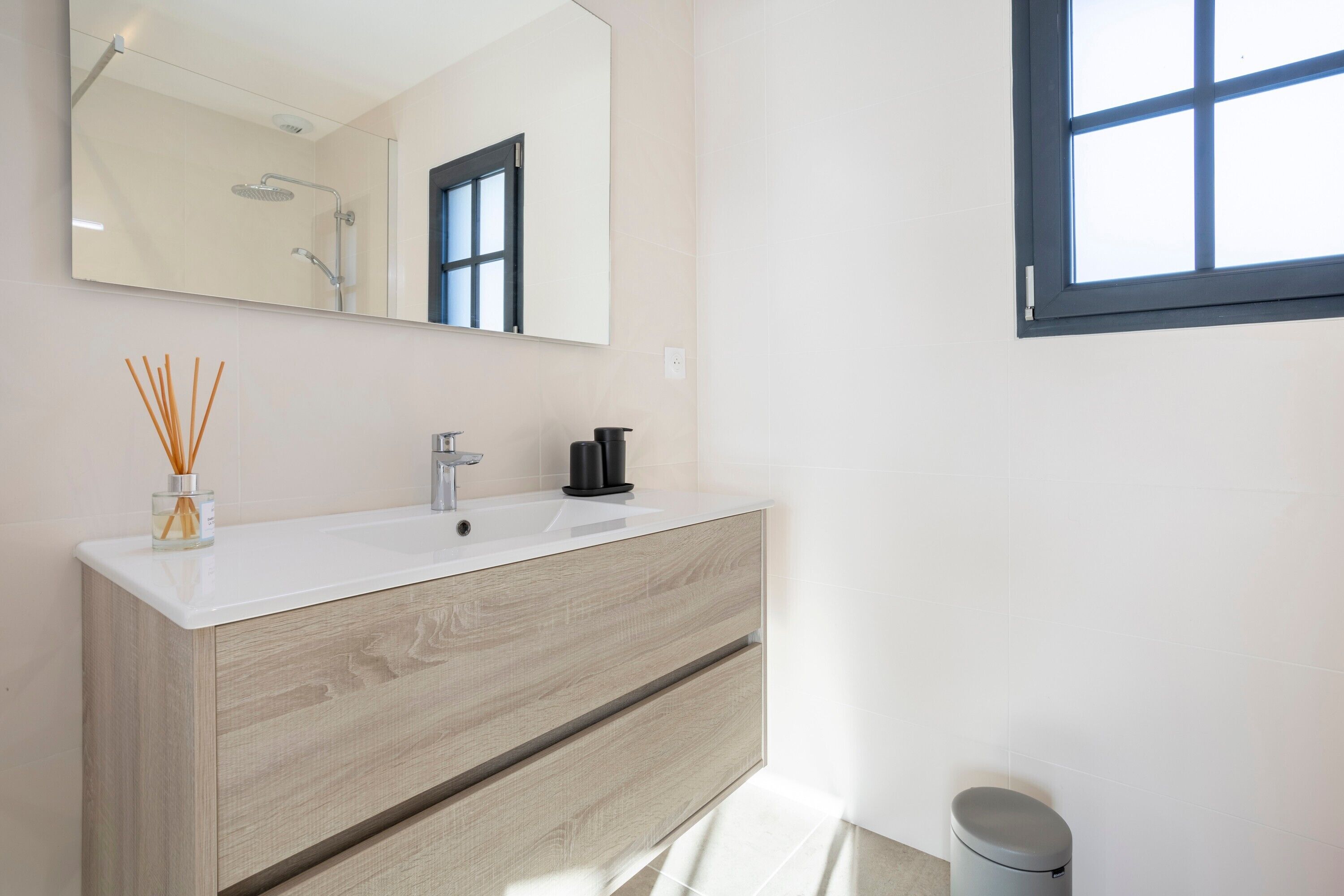 Une salle de bain moderne avec un grand miroir, un lavabo blanc, un meuble-lavabo en bois et une fenêtre.
