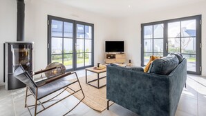 Un salon moderne avec un canapé, un téléviseur, une cheminée et de grandes fenêtres.