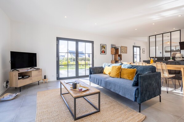 A modern living room with a sofa, coffee table, TV, and a dining area with chairs and a table.