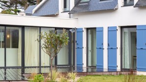 Une maison moderne avec de grandes fenêtres en verre, un petit arbre et une pelouse bien entretenue.