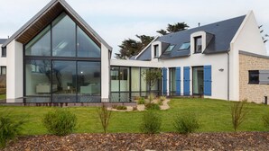 Une maison moderne dotée de grandes baies vitrées, d’un toit en pente et d’une pelouse bien entretenue.