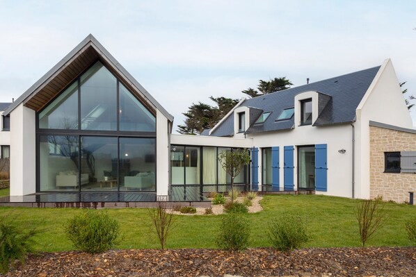 A modern house with large glass windows, a sloped roof, and a well-maintained lawn.