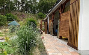 Un edificio con un espacio exterior cubierto, un sendero pavimentado y un paisaje natural con árboles y vegetación.