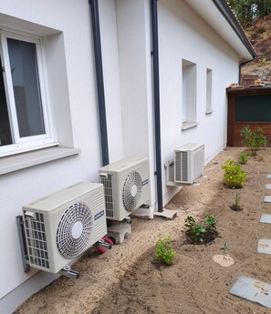 A building with two air conditioning units mounted on the exterior wall, a window, and a small garden area with young plants.