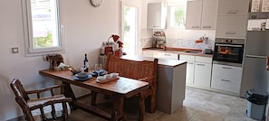 Una cocina con mesa de madera, sillas, estufa y alacenas.