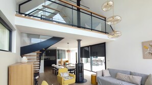 Un interior moderno con comedor, sofá, escalera y vistas al exterior.