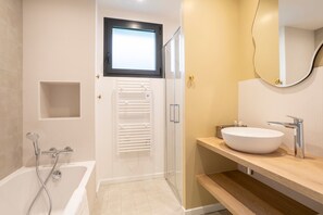 A modern bathroom with a bathtub, shower, and a large mirror above the sink.