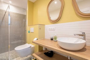 A modern bathroom with a glass shower enclosure, a white toilet, a wooden vanity with a large sink, and two wall-mounted mirrors.