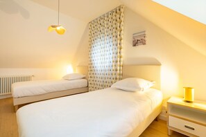 A bedroom with two beds, a nightstand, a lamp, a radiator, and a curtain with a pattern.