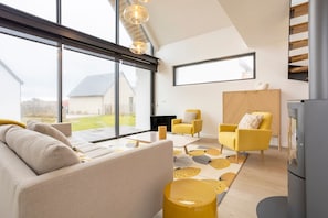 A modern living room with a sofa, yellow chairs, a cabinet, and a large window.