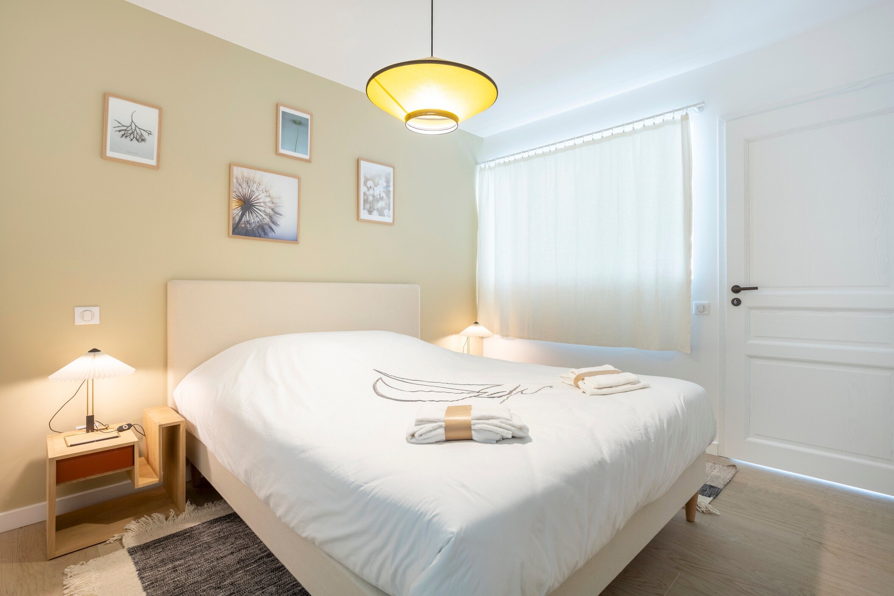 Ein Hotelzimmer mit einem Bett, Nachttischlampen, einer Tür und gerahmten Bildern an der Wand.