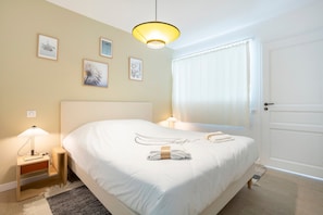 A hotel room with a bed, bedside lamps, a door, and framed artwork on the wall.