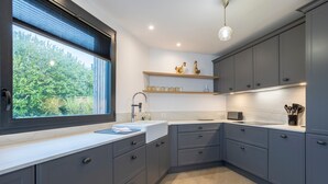 Una cocina moderna con armarios grises, encimera blanca, ventana con persianas y una lámpara colgante.