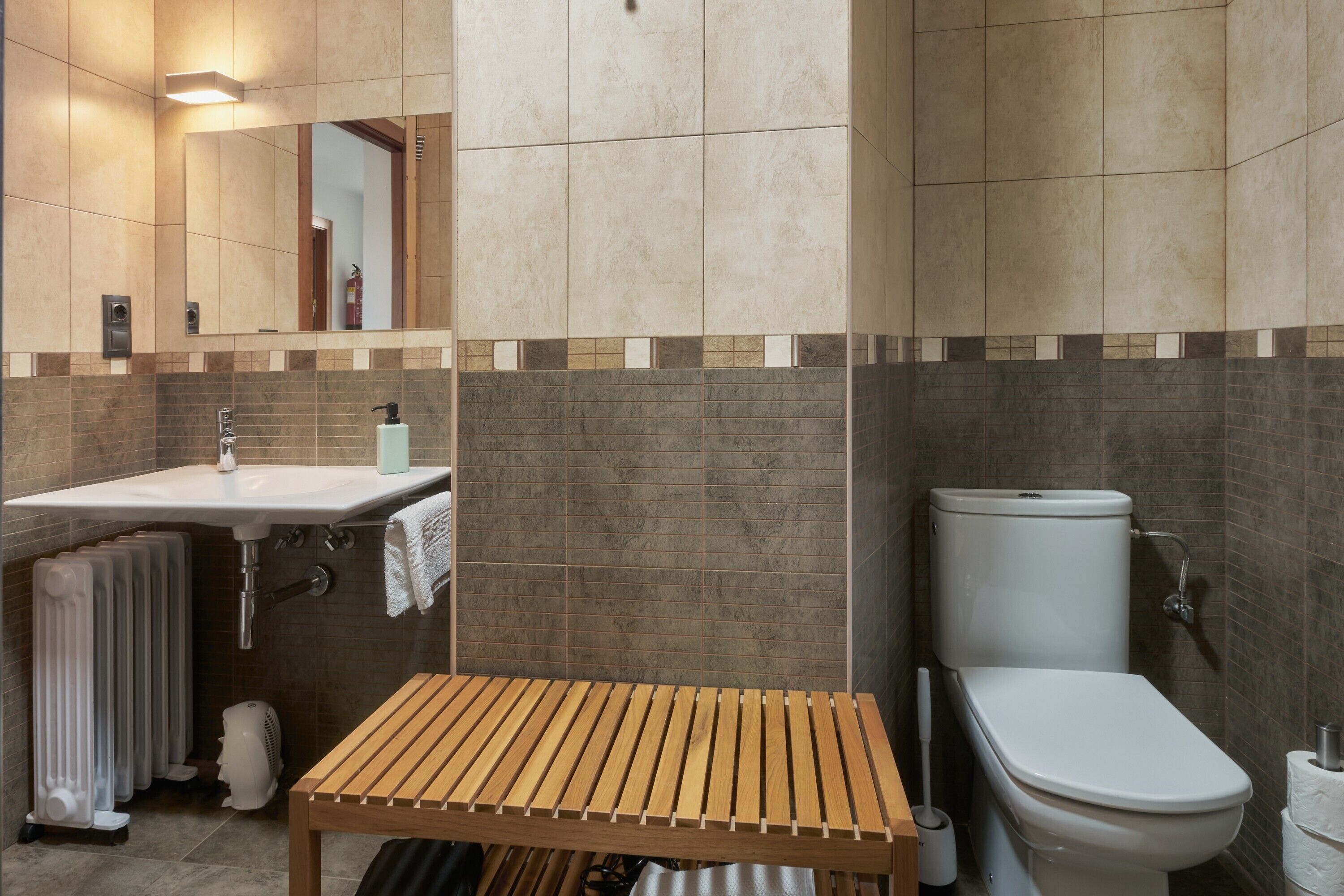 Un baño con lavamanos, inodoro, espejo y un banco de madera.
