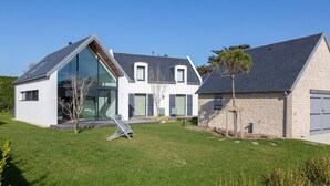 Une maison moderne à deux étages, dotée d’une grande baie vitrée, d’une façade en pierre et d’une pelouse bien entretenue.