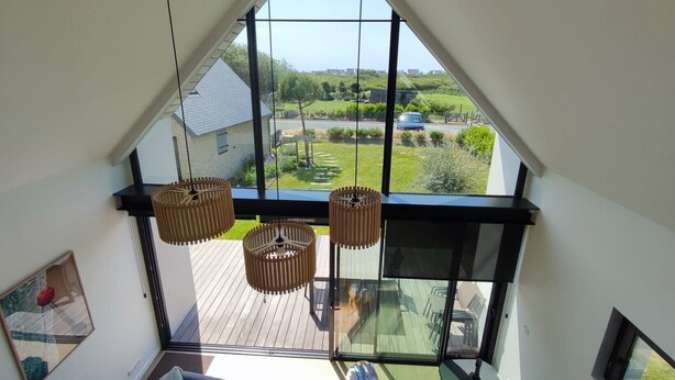 Une chambre de style loft moderne, dotée de grandes fenêtres, d’une terrasse en bois et offrant une vue sur un paysage verdoyant.