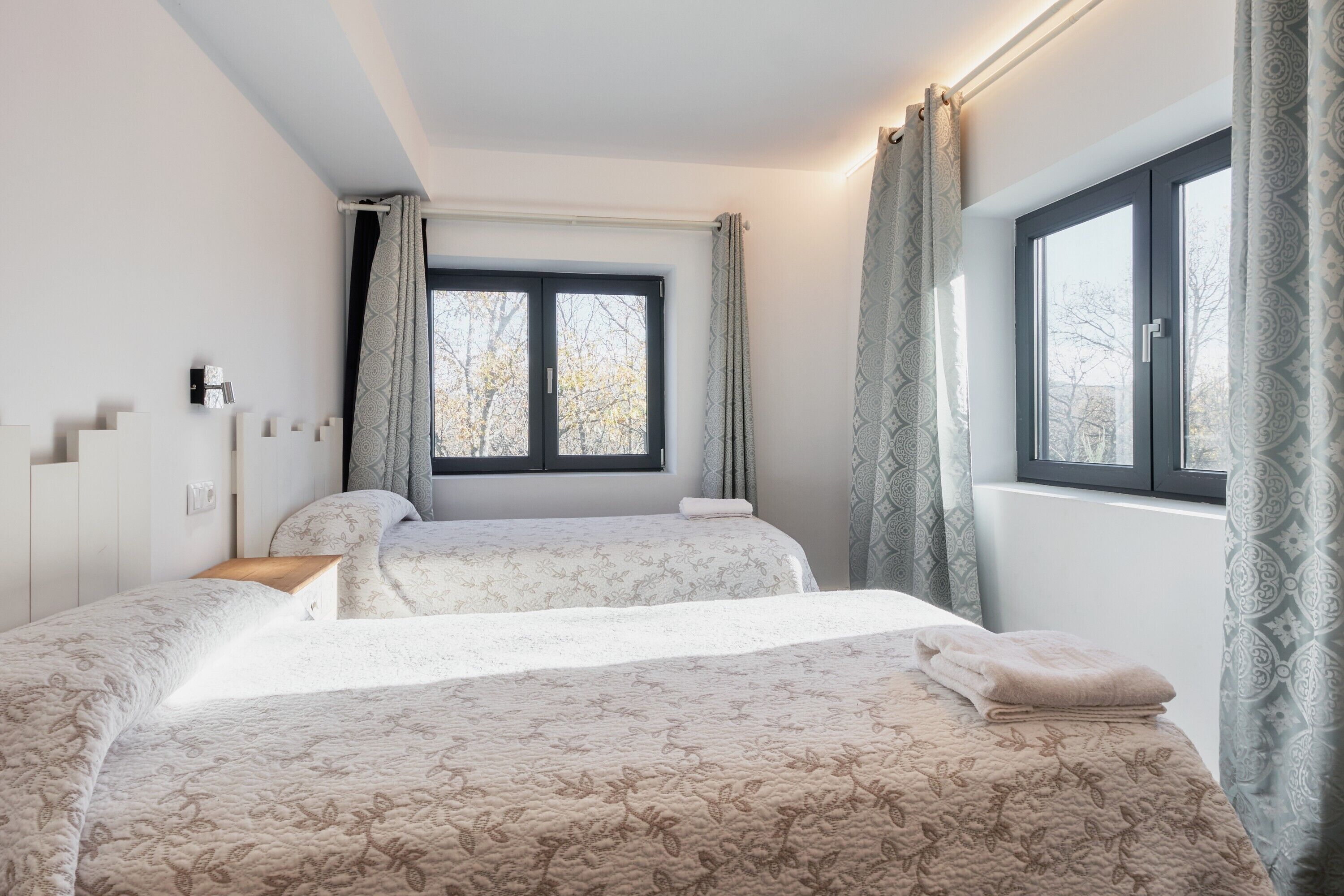 Een slaapkamer met twee bedden, een raam met gordijnen en een nachtkastje.