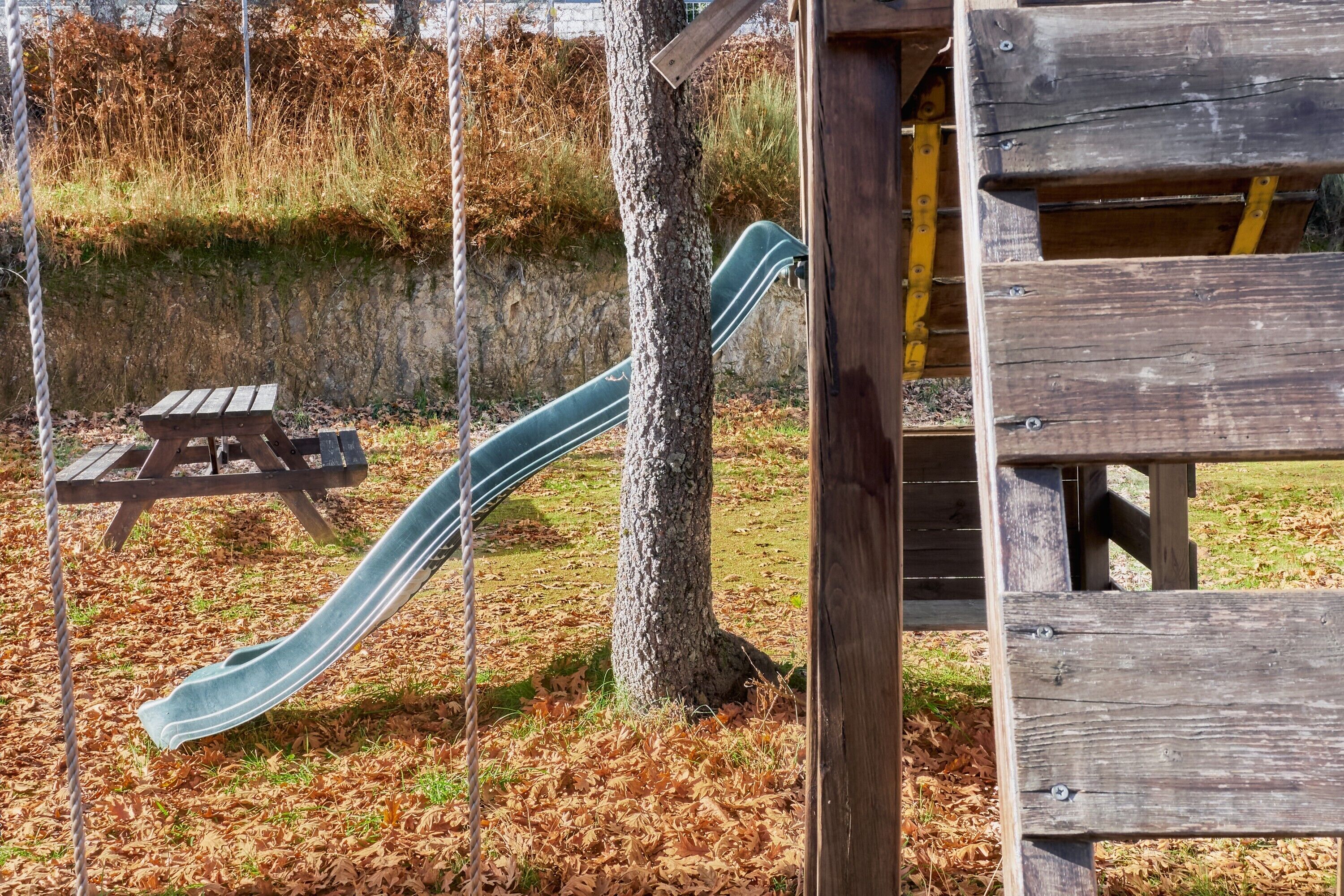 Une aire de jeux avec un toboggan, une table de pique-nique et une structure en bois.