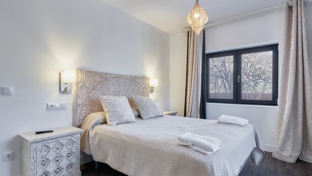 A neatly arranged bedroom with a bed, bedside lamps, a nightstand, and a window with curtains.