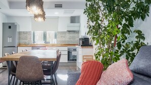 A modern kitchen with a dining area, a sofa with cushions, and a potted plant.