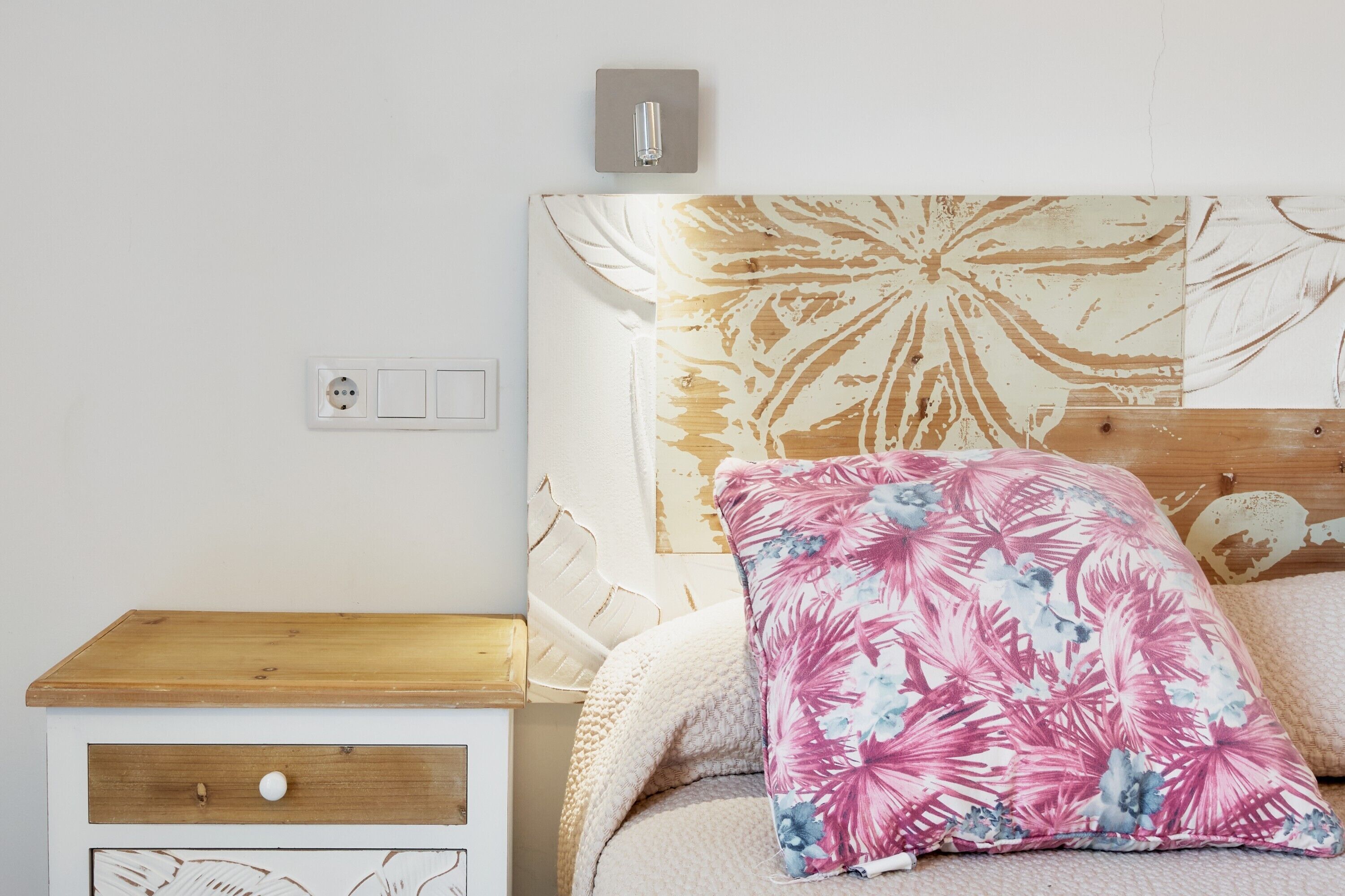 Ein Schlafzimmer mit einem hölzernen Nachttisch, einem Bett mit Blumenbord und einer Steckdose.