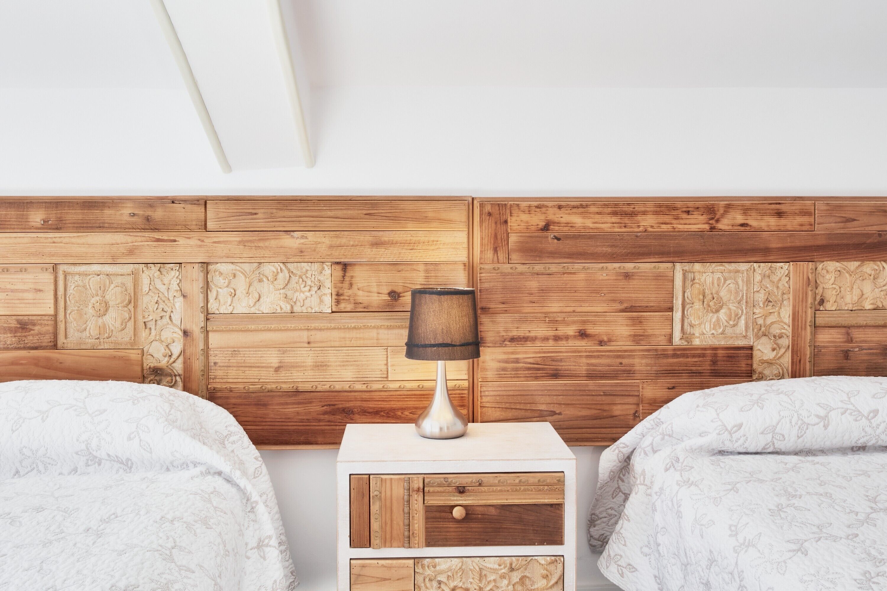 Une chambre avec deux lits, une table de chevet avec une lampe et une tête de lit en bois.
