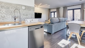 A modern kitchen with a dishwasher, a grey sofa, and a dining table with chairs. - Apartment 'Marel' with Mountain View, Wi-Fi and Air Conditioning (Cerdillo de Sanabria)