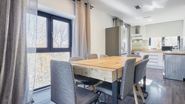 A modern kitchen with a wooden table and chairs, a refrigerator, and a window with curtains. - Apartment 'Marel' with Mountain View, Wi-Fi and Air Conditioning (Cerdillo de Sanabria)