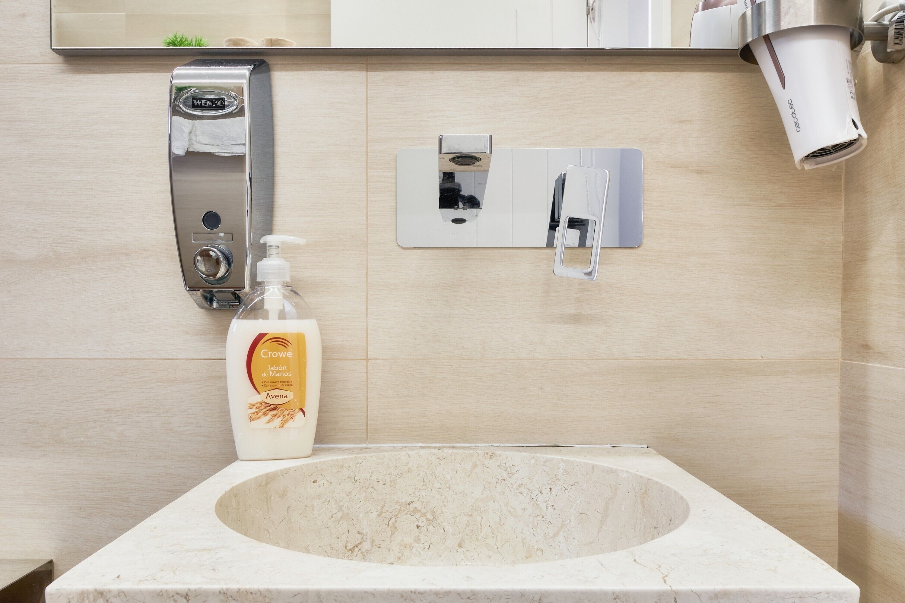 Un bagno con lavabo in marmo, un dispenser per sapone liquido, un dispenser per asciugamani di carta e uno specchio.