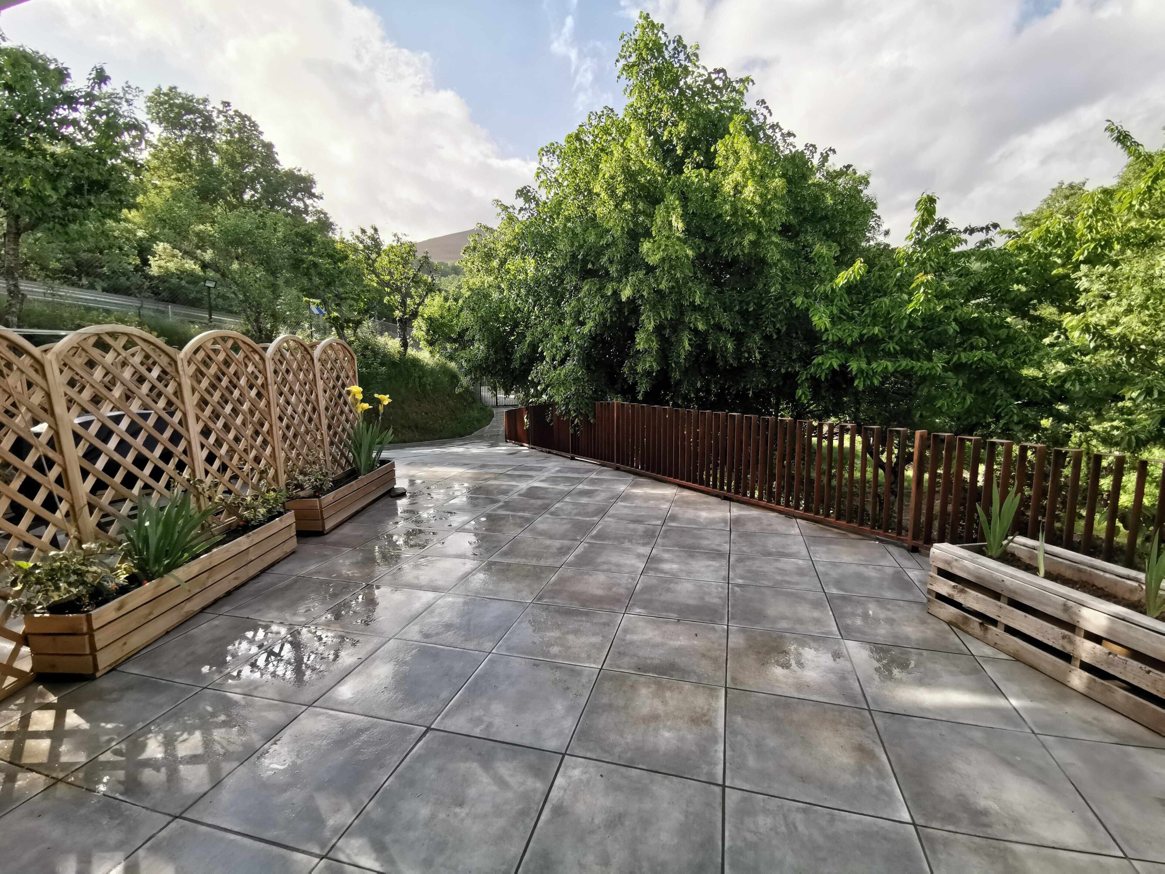Un'area esterna pavimentata con fioriere in legno e una recinzione in metallo.