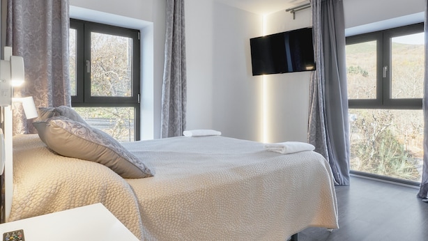 A bedroom with a large bed, a flat-screen TV mounted on the wall, and a window with curtains. - Apartment 'Marel' with Mountain View, Wi-Fi and Air Conditioning (Cerdillo de Sanabria)