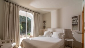 Quarto com uma cama, uma cadeira, mesa de cabeceira e janela com cortinas.