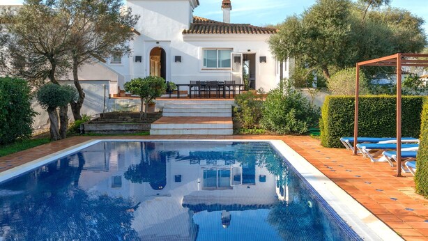 Vista da piscina de uma casa, com piscina, um alpendre com cadeiras e um jardim.