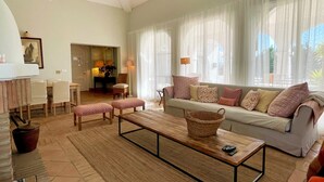 Uma sala de estar com sofá, mesa de centro, um banco e um espaço de jantar com cadeiras.