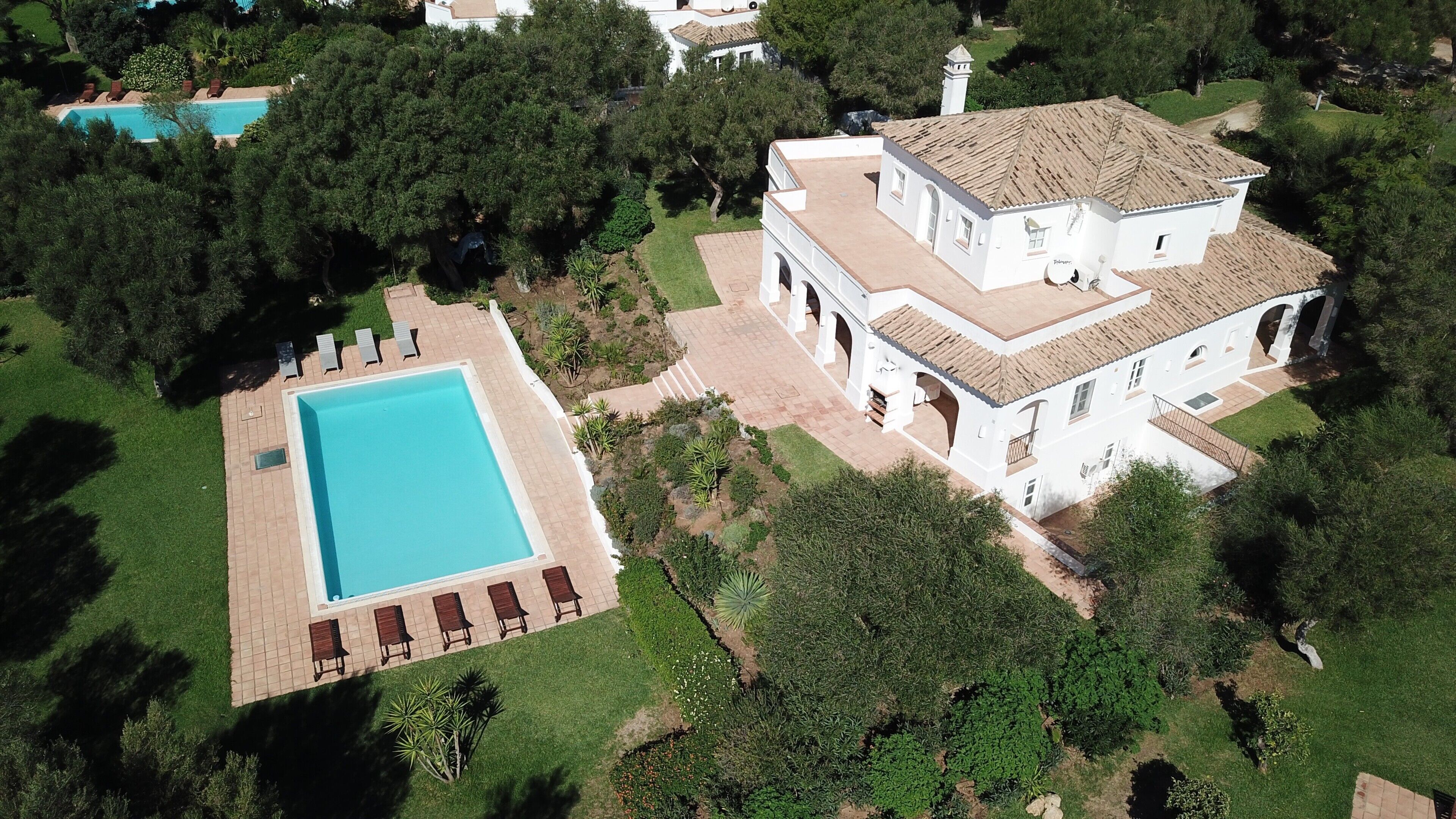 Vue aérienne d’une propriété dotée d’une piscine, d’un grand bâtiment blanc surmonté d’un toit en tuiles et entouré de verdure.
