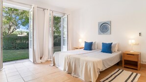 A bedroom with a bed, two bedside tables, a nightstand, a window with curtains, and a view of greenery outside. - Holiday Home 'Birdie' with Private Pool, Wi-Fi, and Air Conditioning (Benalup-Casas Viejas)