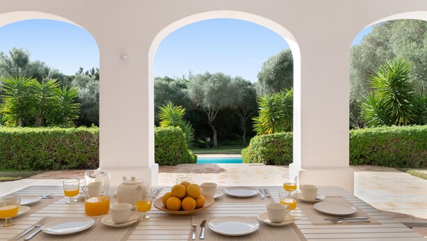 A breakfast setup with a table, plates, cups, and a pitcher of orange juice, overlooking a pool and greenery. - Holiday Home 'Birdie' with Private Pool, Wi-Fi, and Air Conditioning (Benalup-Casas Viejas)
