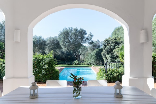 Blick auf einen Pool, mit weißer Pergola und üppiger, grüner Bepflanzung.