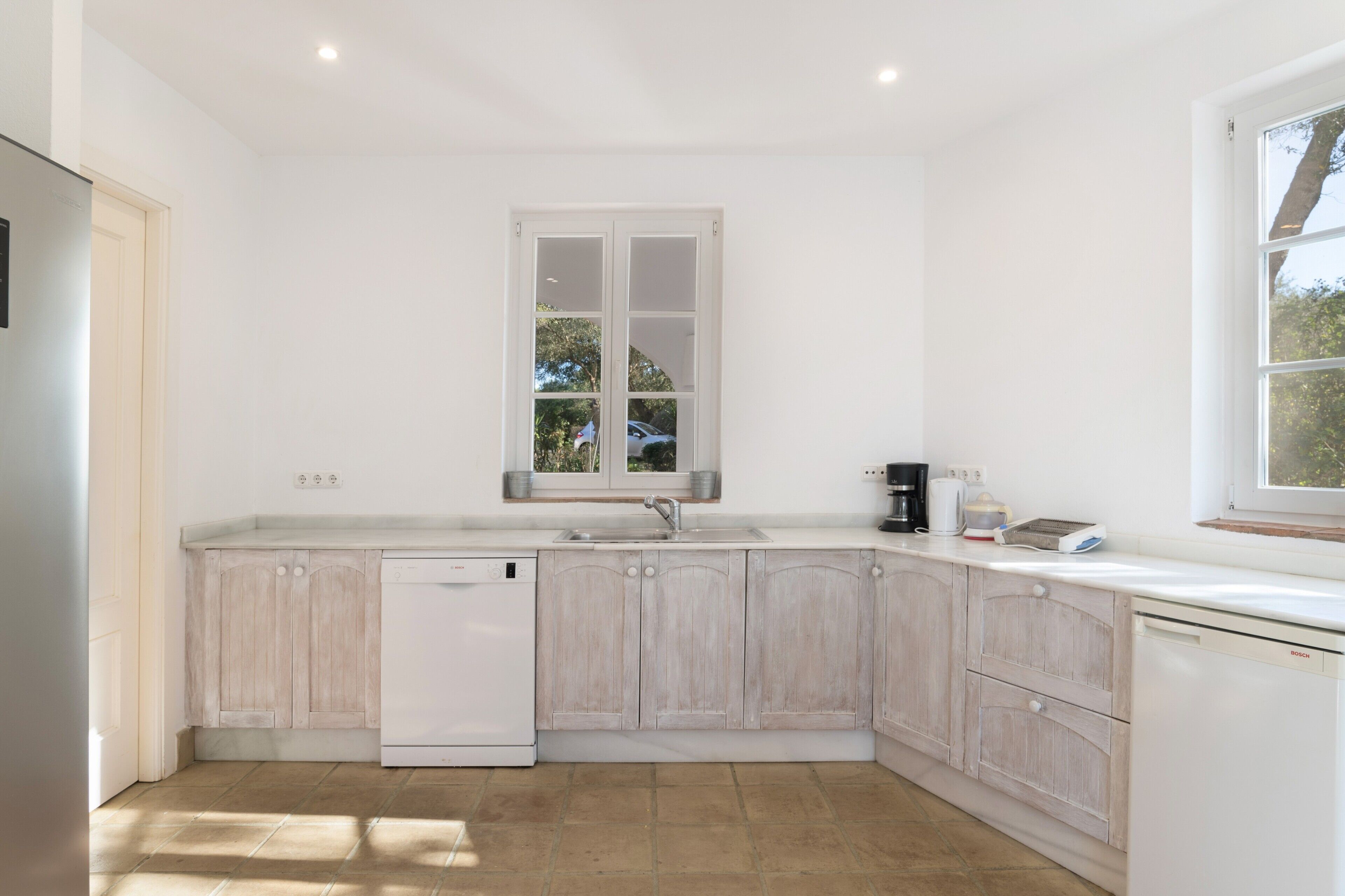 Una cocina moderna con armarios blancos, lavavajillas integrado, una ventana sobre el fregadero y una encimera con cafetera.