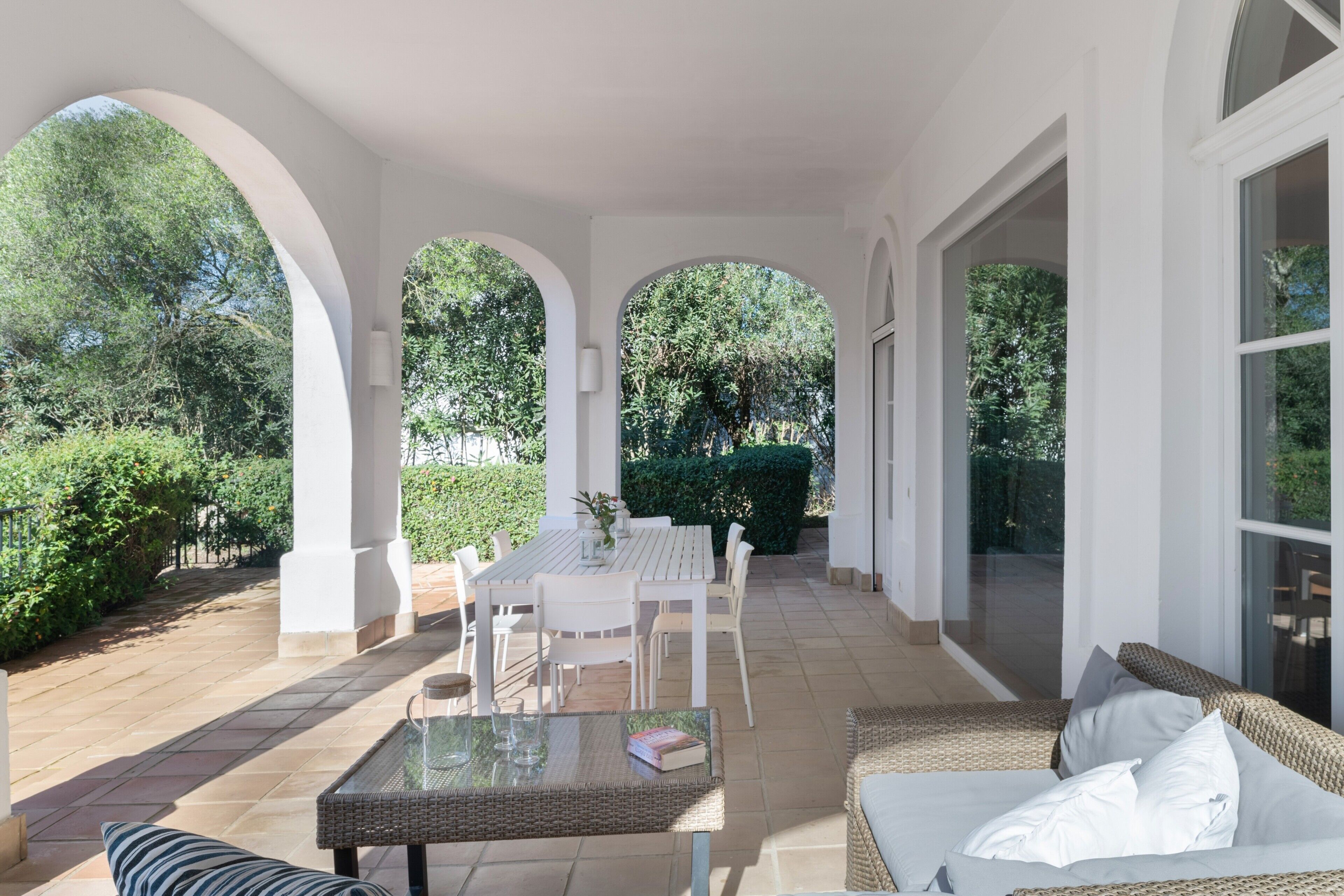 An outdoor patio area with a white table and chairs, a wicker sofa, and a glass-top coffee table.
