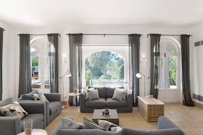 Ein Wohnzimmer mit einer grauen Sofagarnitur, einem Couchtisch und Blick durch ein großes, rundes Fenster.