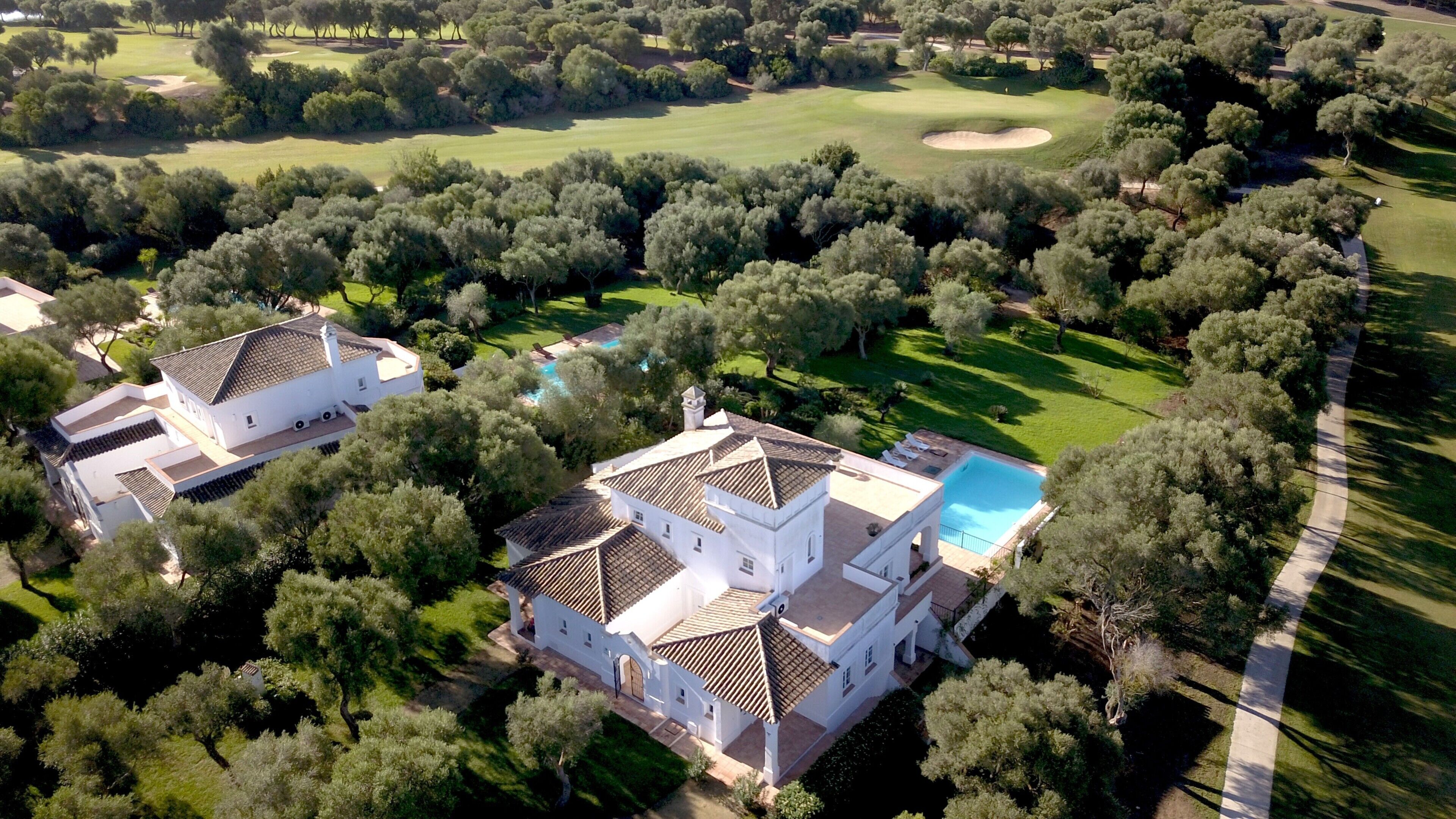 Vue aérienne d’une propriété comprenant deux bâtiments blancs, une piscine et, au loin, un terrain de golf.