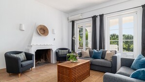 Una sala de estar con chimenea, dos sofás, una mesa de centro y ventanas grandes con cortinas.