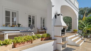 Un edificio blanco con un patio que tiene una mesa, sillas y una parrilla.