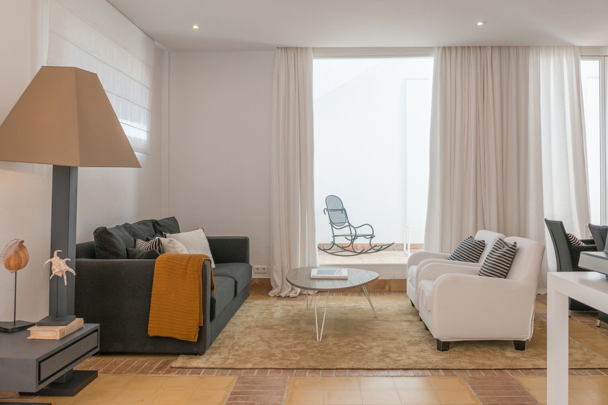 Un salón moderno con sofá, sillones, una mesa de centro, una lámpara y vistas al exterior.