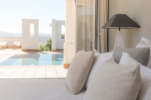 Een slaapkamer met een bed, kussens, een lamp en uitzicht op een zwembad en terras.
