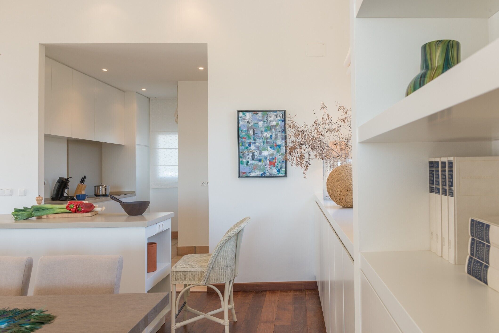 Una cocina moderna con armarios blancos, un comedor con mesa y sillas, y un adorno en la pared.