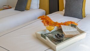 A neatly made bed with a tray of breakfast items, including a drink, book, and fruits.